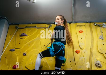 Young woman climbing a tall, indoor, man-made rock climbing wall Stock Photo