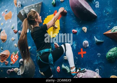 Young woman climbing a tall, indoor, man-made rock climbing wall Stock Photo