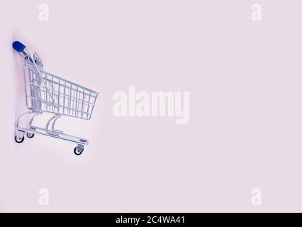 empty shopping cart over light pink background, mini metal cart isolated on color background Stock Photo