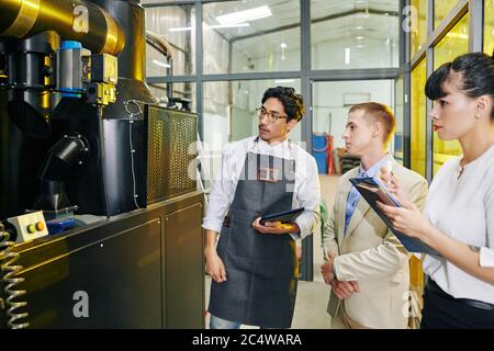 Modern coffee roastery owner in apron showing equipment to inspectors Stock Photo