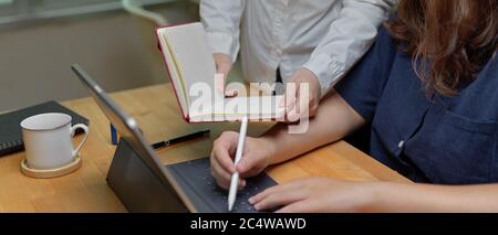 Cropped shot of two female employees briefing on their project with mock-up tablet and blank notebook Stock Photo