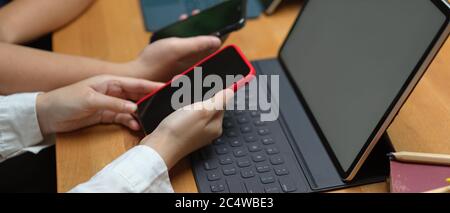 Side view of female college students surfing internet on smartphone to find informations for their project while working working with tablet in librar Stock Photo
