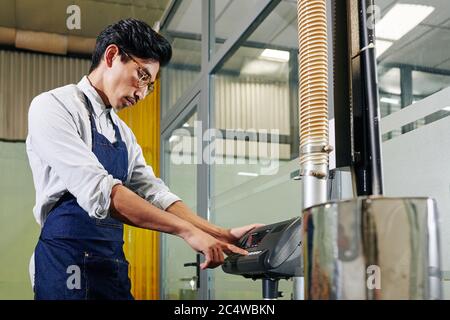 Serious small business owner pushing button on coffee roaster machine control panel Stock Photo