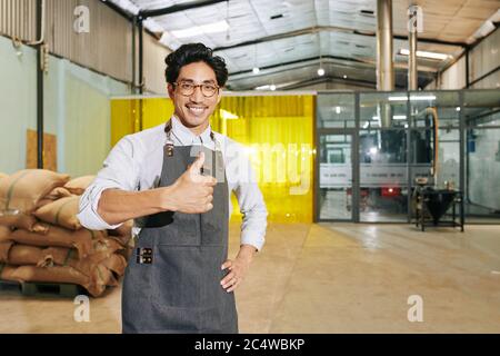 Portrait of cheerful coffee roastery owner showing thumbs-up and smiling at camera when standing in warehouse Stock Photo