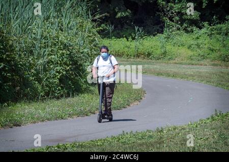 A young man wearing a surgical mask rides his scooter on a path in Kissena Park in Flushing, Queens, New York City. Stock Photo