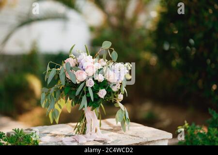 bridal bouquet of pink and lavender roses, branches of eucalyptus tree, delphinium, veronica and pink ribbons on the stone fence Stock Photo