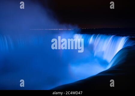 Niagara Falls illuminated in blue light with rainbows from the mist Stock Photo