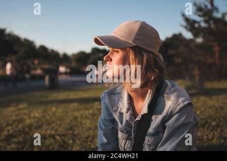 Beautiful blonde girl in a cap with short hair sits and looking away. Selective focus. Stock Photo