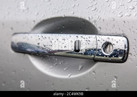 Chrome-plated Car door handle with keyhole and remote keyless opening button cover the water droplets after the rain, side view sharpness on the black Stock Photo
