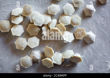 Pelmeni dumplings lie on a cutting board, sprinkled with gray flour, top view. Stock Photo