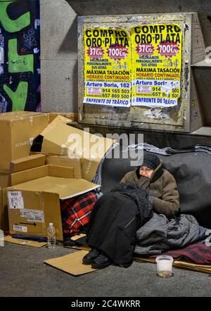 A homeless woman sleeping rough in the street, below posters advertising the purchase gold and silver, central  Madrid, Spain. Stock Photo