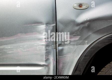 scratched car door and fender after an accident, close up car body damage scratches and blow in the side of the gray car. Stock Photo