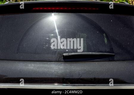 Rear window of a black dirty car covered in dust with a sun flare. Stock Photo