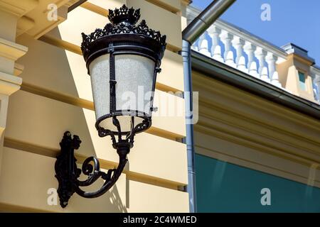 Lantern mounted on the wall of the facade of the building, iron illuminated forged patterns. Stock Photo