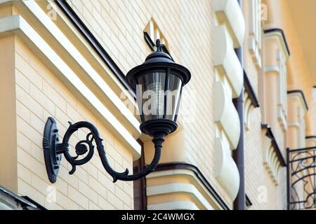 Black iron wall lamp mounted on the facade of a yellow brick building. Stock Photo