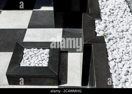 the exterior is a building with square paving slabs and marble beds on the ground and on a black marble wall decorated with white round pebbles. Stock Photo
