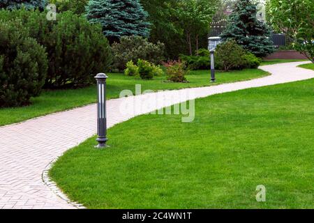 Sidewalk in the backyard of the mansion with green lawns, bushes and pine trees. Stock Photo