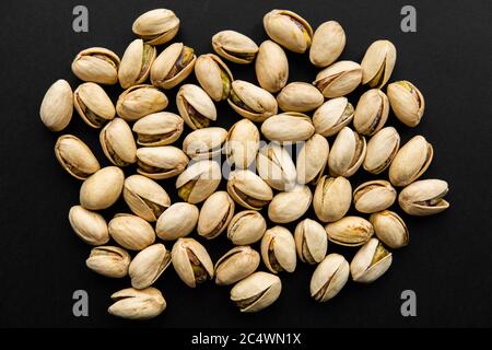 Pistachios scattered on a black table. Pistachio is a healthy vegetarian protein nutritious food. Natural nuts snacks. Stock Photo