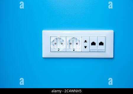 a socket on a light blue wall, a multiple outlet with an internet connection, two European type and one American type outlet. Stock Photo