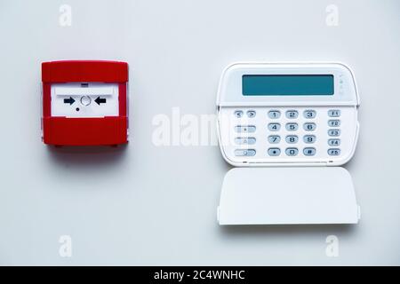 Fire safety button in a red box on a gray wall near a white alarm control panel with security password input buttons, front view on a bright wall indo Stock Photo