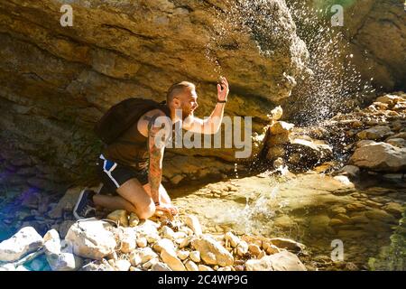 Hiker drinking water from the river. Man enjoys clean fresh unpolluted water in the mountain creek Stock Photo