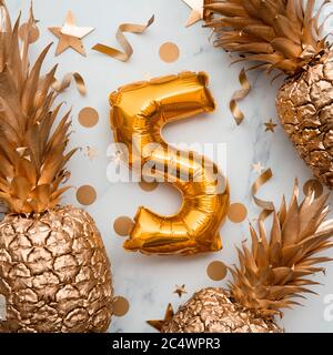 5th birthday celebration card with gold foil balloons and golden pineapples Stock Photo