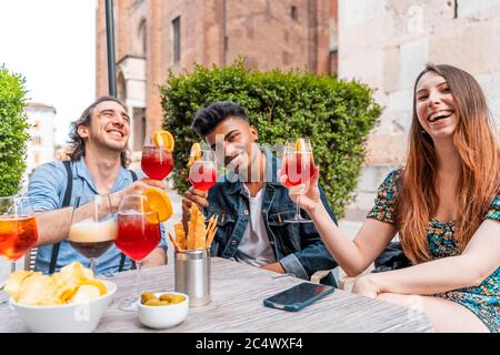 Friends drinking colored cocktail at outdoor bar - New normal lifestyles concept with happy people toasting drinks outside Stock Photo