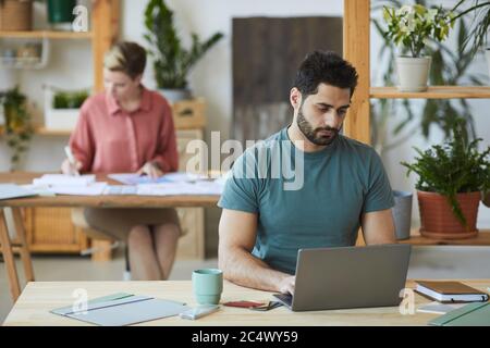 Portrait of handsome bearded man using laptop while working at wooden desk in office, copy space Stock Photo