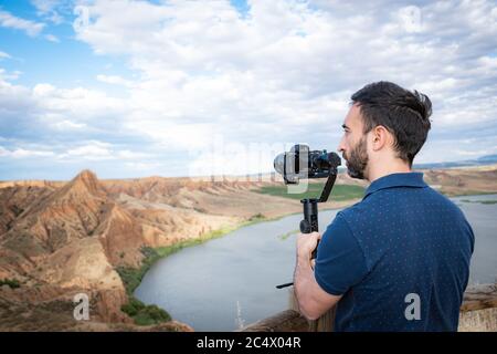 young filmmaker filming natural landscape in canyon with a large river and marshes Stock Photo