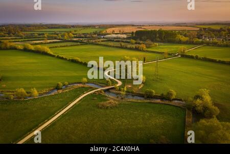 Aerial view of a winding dirt road across meadows and a bridge over the river Stock Photo