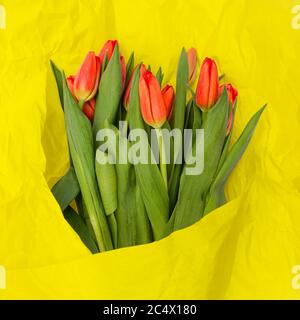 Bunch of tulips wrapped in yellow paper. Beautiful flowers for the holiday. Romantic bouquet and crumpled paper texture Stock Photo