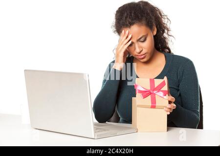 unhappy african woman at the desk with a laptop opens a box with a gift Stock Photo