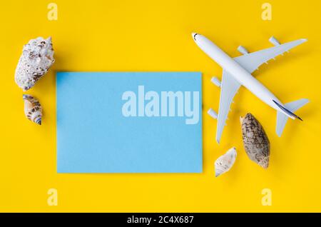 Empty blue paper on yellow background with seashells and decorative airplane. Summer travel concept. Top view or flat lay. Copy Space. Stock Photo