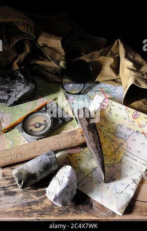 Geological instruments (cards, hammer, notebook, mountain compass, magnifying glass) on a wooden table Stock Photo