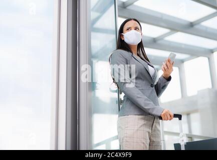 Businesswoman with smartphone going on business trip, wearing face masks at the airport. Stock Photo