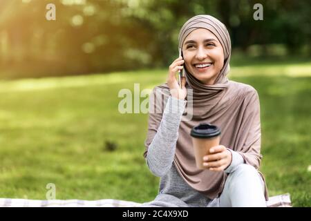 Happy muslim girl talking on phone and drinking coffee Stock Photo