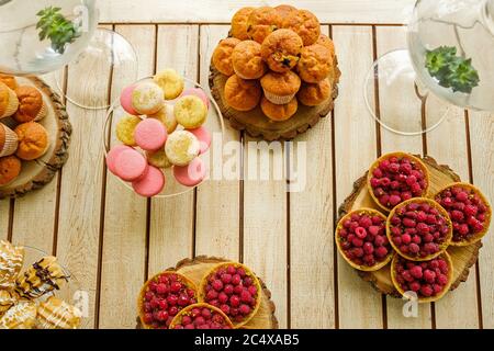 Flat view of tasty desserts on a wooden table. Muffins, macarons, raspberry tarts and cookies Stock Photo