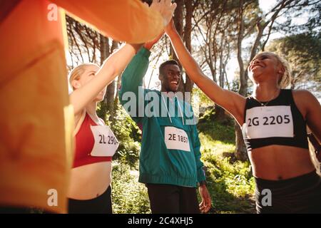 Group of runners giving high five each other. Multi-ethnic group of men and women celebrating after finishing the race. Stock Photo