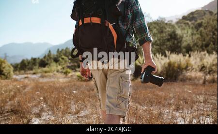 Rear view of a senior man carrying a backpack hiking in nature holding a digital camera. Man on hiking trip.