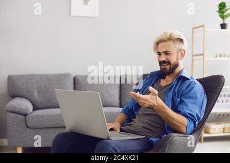Guy talking online home. Cheerful male freelancer talking on video chat via laptop. Stock Photo