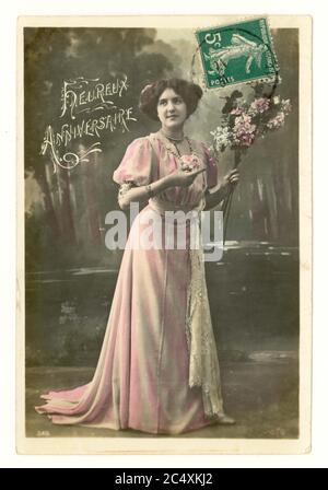 Early 1900's French sentimental tinted greetings postcard of a pretty woman in a long flowing summer dress holding a bouquet of flowers - the message is 'Happy Anniversary', France, circa 1911 Stock Photo