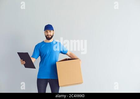 Deliveryman holding clipboard and carton parcel box with space for design on grey background. Online postal service Stock Photo