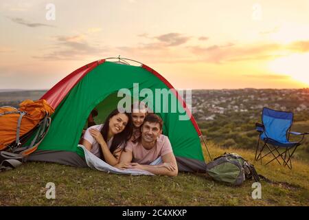 Happy family with child on camping trip relaxing inside tent. Caring parents and their daughter relaxing at campsite Stock Photo