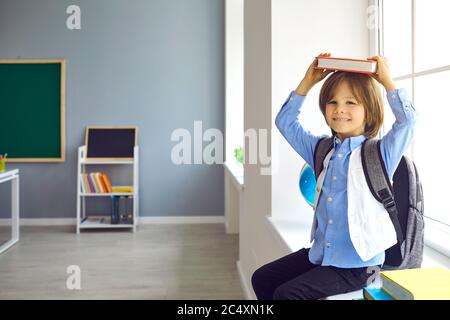 Cute schoolboy holds a book over his head in a school class. First time at school. Stock Photo