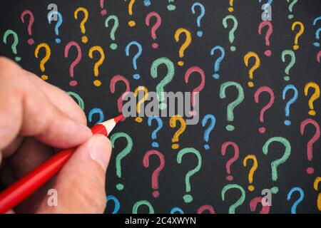 Man drawing colorful question marks with a pencil on black paper. Close up. Stock Photo