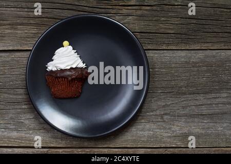 A cupcake, topped with whipped cream and decorated with a button-shaped candy, it was cut vertically and placed on a plate on weathered wood planks. Stock Photo