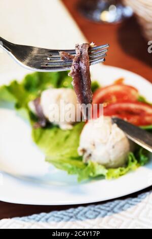 Anchovy on fork with smoked fish pate and salad appetizer in background. Mediterranean cuisine, gourmet food and travel concepts Stock Photo