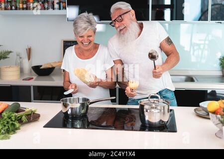 Happy senior couple dancing while cooking together at home - Mature people having fun preparing the lunch - Joyful elderly lifestyle and food nutritio Stock Photo
