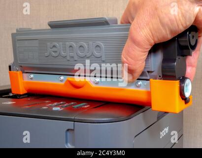 A man’s hand on a replacement Brother toner ink cartridge for the Brother laser printer below. Stock Photo