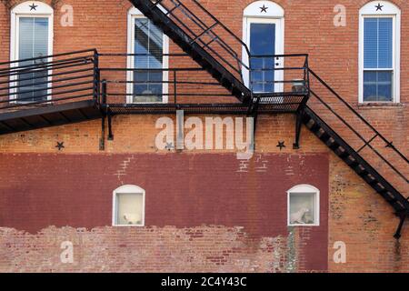 arched white windows behind back alley fire escape stairs at an old faded brick building Stock Photo